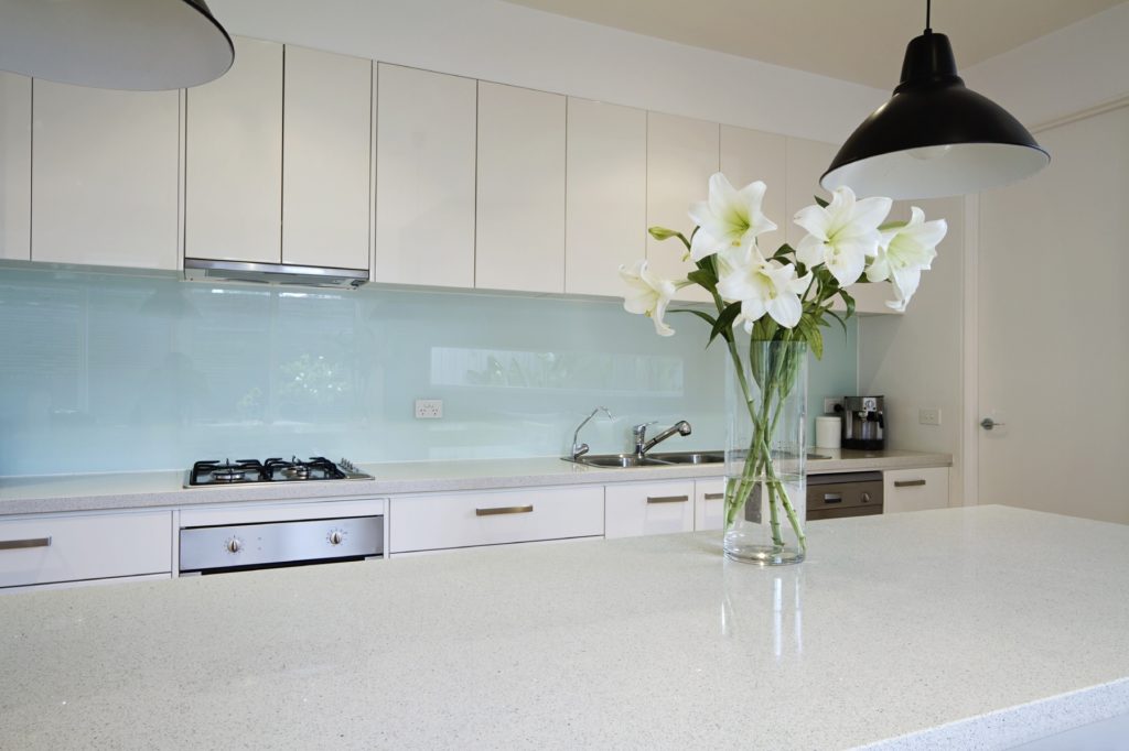 Современный дизайн интерьера кухни с одноцветным стеклянным фартуком.